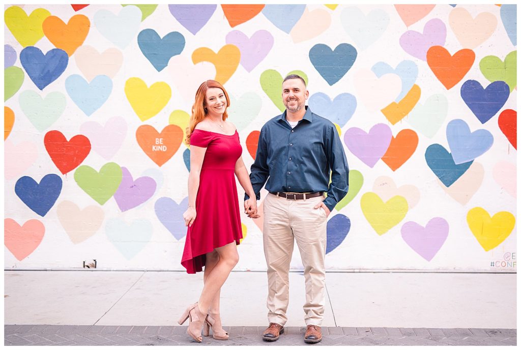 Couple holding hands at the Confetti Hearts Wall in Charlotte, NC, by Charlotte engagement photographer, Jacqueline Jones