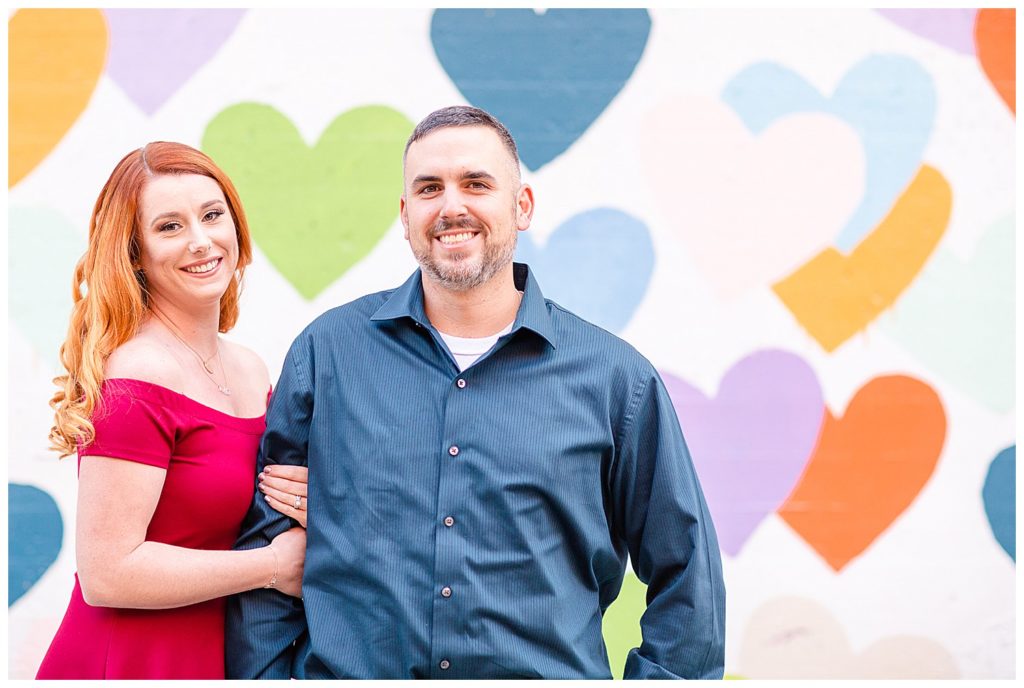 Woman holding man’s arm at the Heart Confetti Wall in Charlotte, NC, by Charlotte engagement photographer, Jacqueline Jones