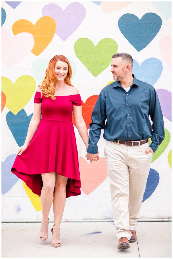 Engaged couple standing at the Heart Confetti Wall in Charlotte, NC, by Charlotte engagement photographer, Jacqueline Jones