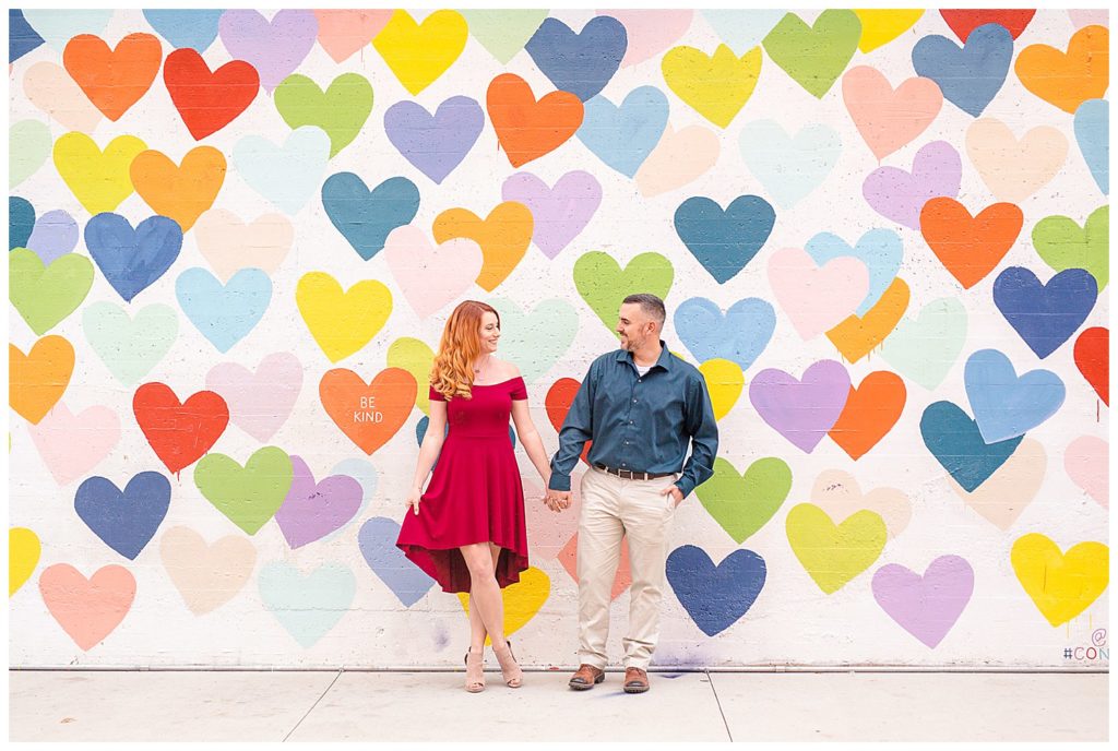 Engaged couple standing and holding hands at the Heart Confetti Wall in Charlotte, NC, by Charlotte engagement photographer, Jacqueline Jones