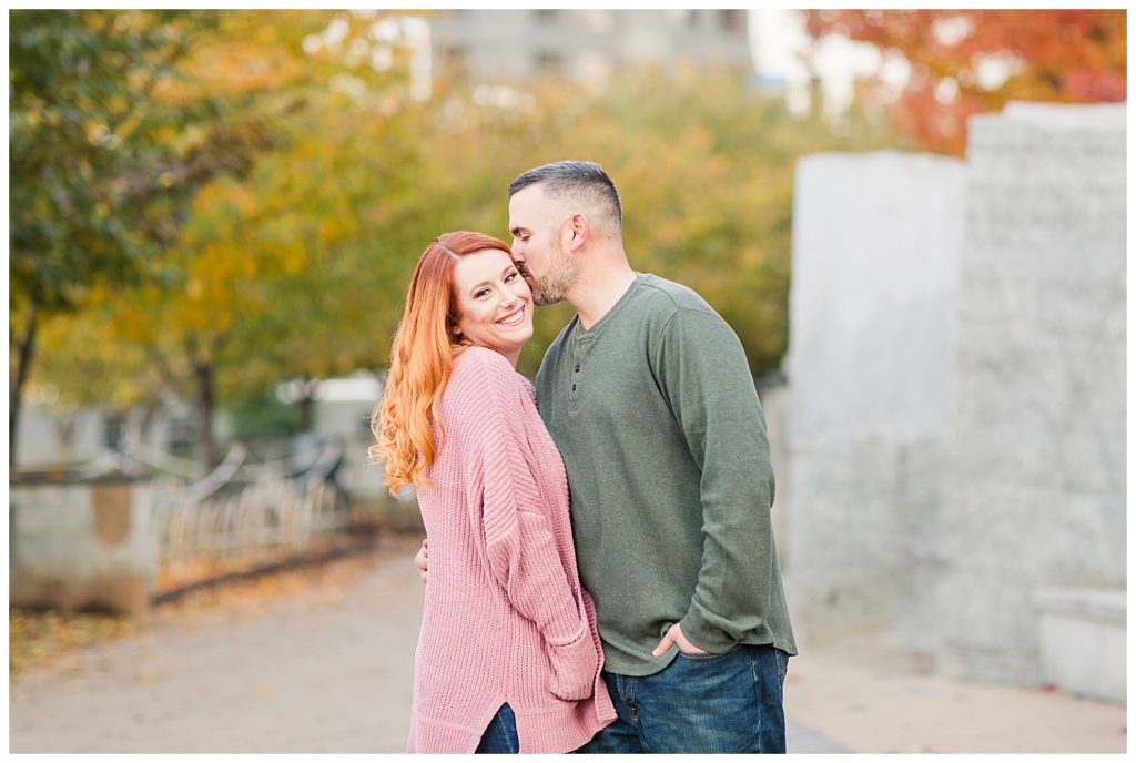 Engaged woman being kissed by fiancé at the Romare Bearden Park in Charlotte, NC, by Charlotte engagement photographer, Jacqueline Jones