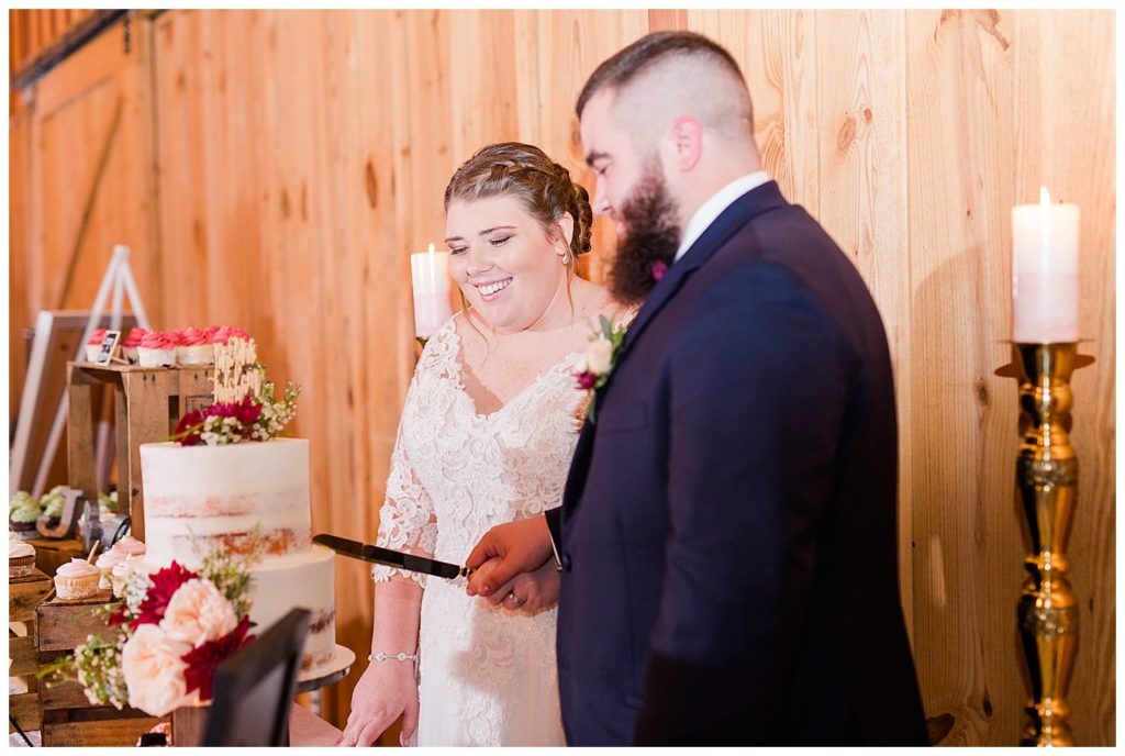 Bride and groom cutting the naked-style wedding cake at the Barn at Sandcastle Farm in Dallas, NC by Charlotte wedding photographer, Jacqueline Jones